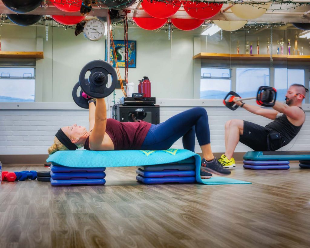 People lifting weights with a bar on a yoga mat