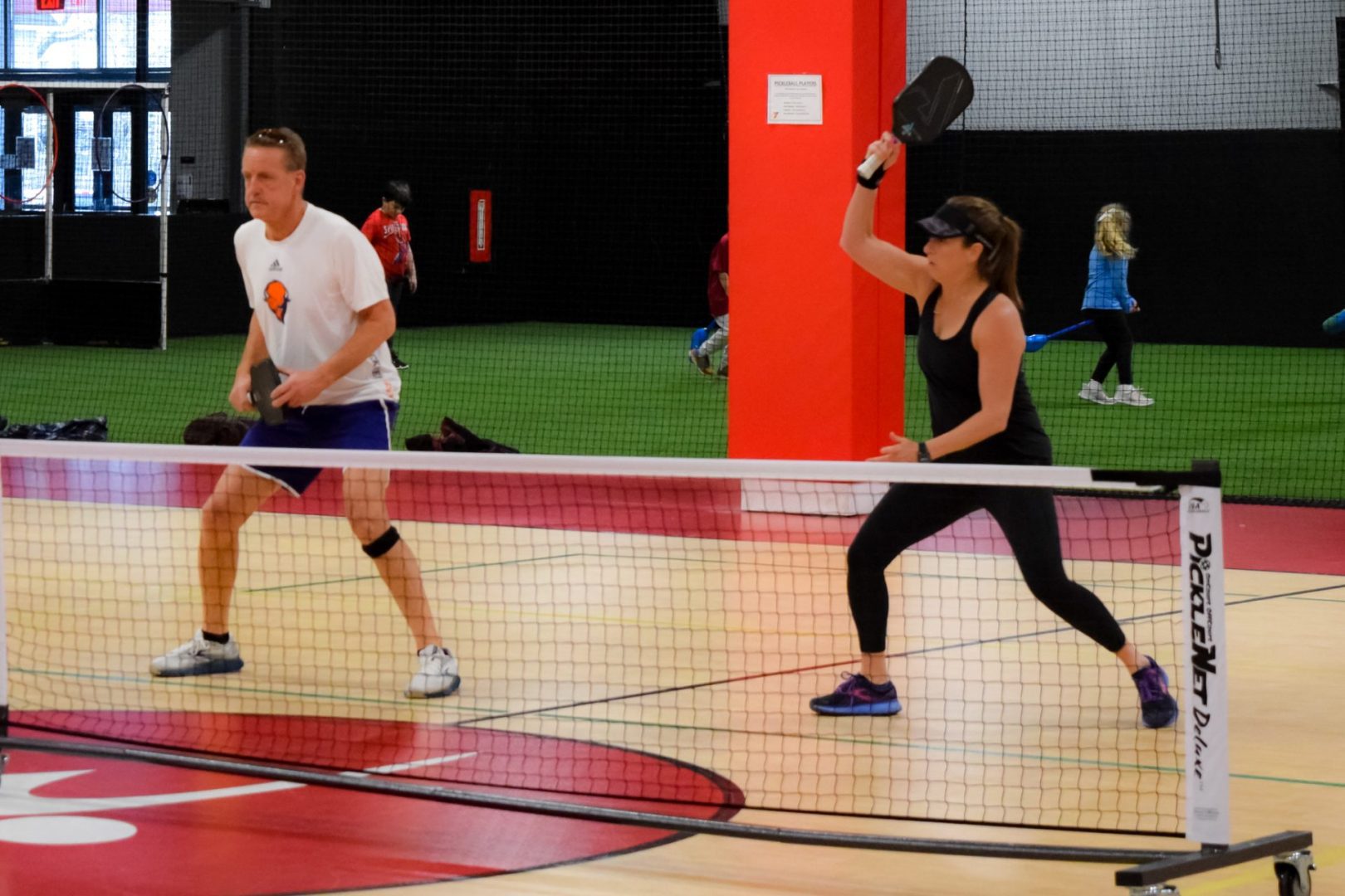 A mixed doubles couple playing pickleball with a player returning a serve