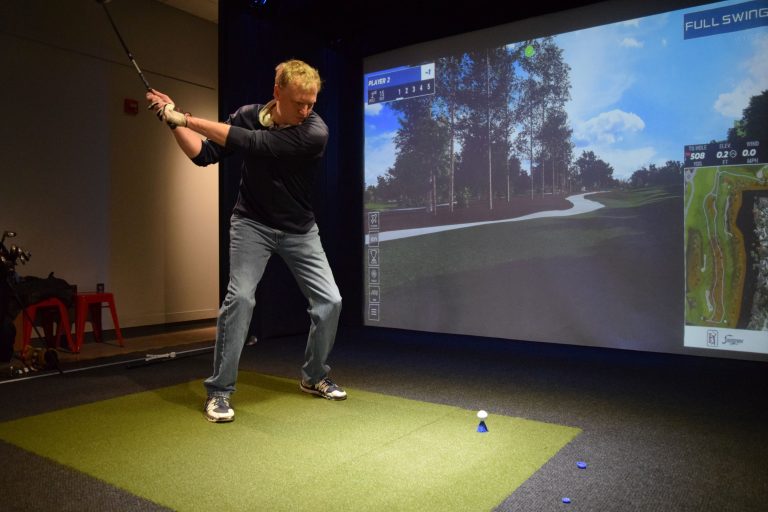 A golf simulator player in his backswing teeing off on a hole.
