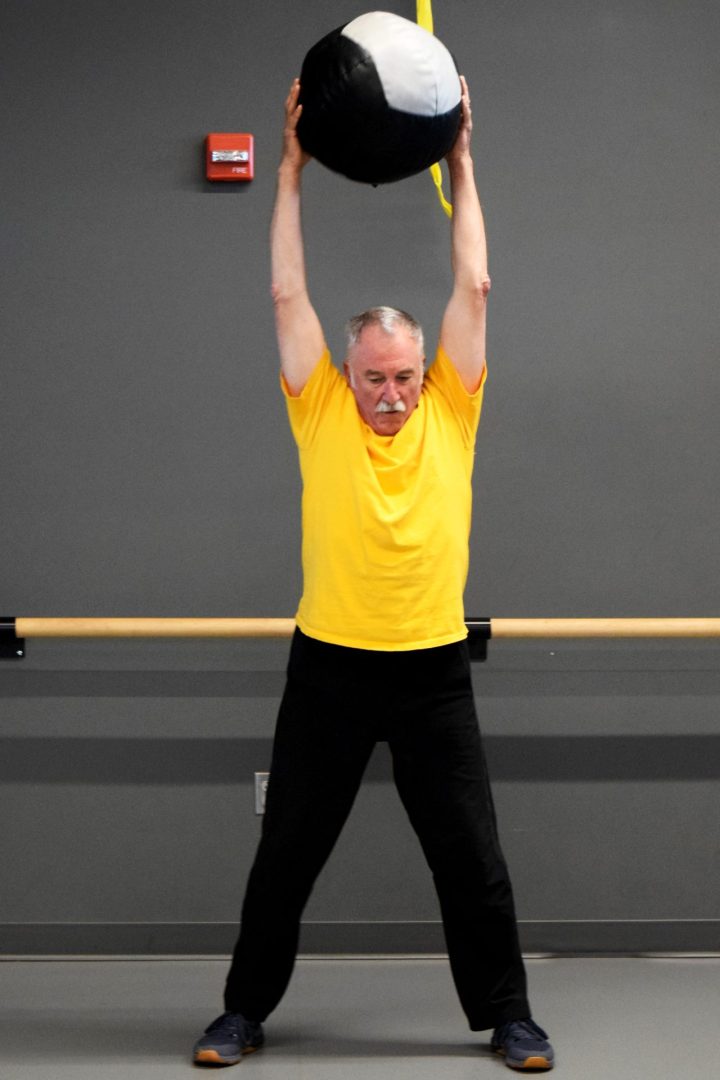 Functional Fitness – 01 Class participant holding a medicine ball above their head, ready to throw it onto the floor.